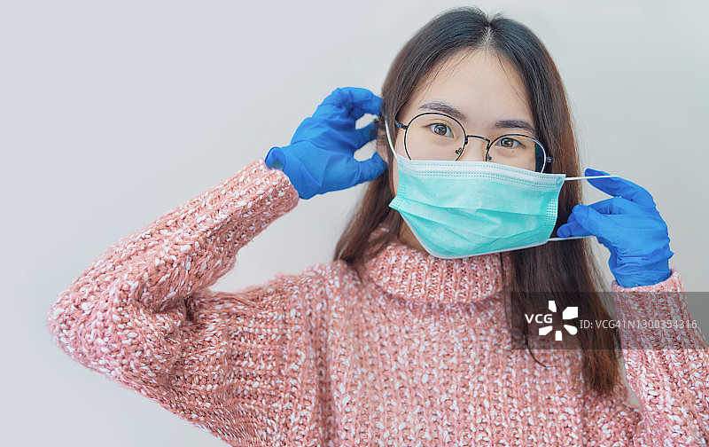 COVID-19冠状病毒大流行。快乐的亚洲女性积极与希望戴着外科口罩和蓝色防护服在家。激发对未来的信心，解决危机。图片素材