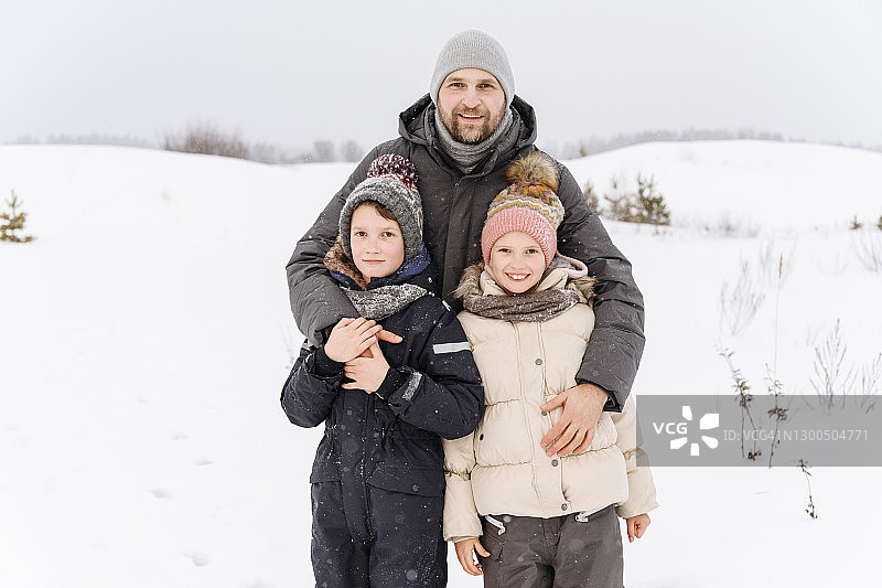 微笑的父亲和孩子们站在白雪覆盖的风景对天空图片素材