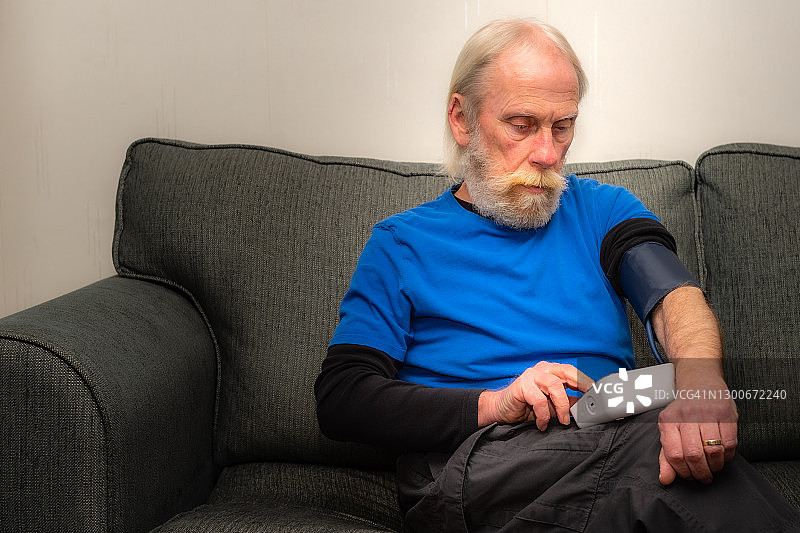 一位老人坐在家里的沙发上检查他的血压图片素材