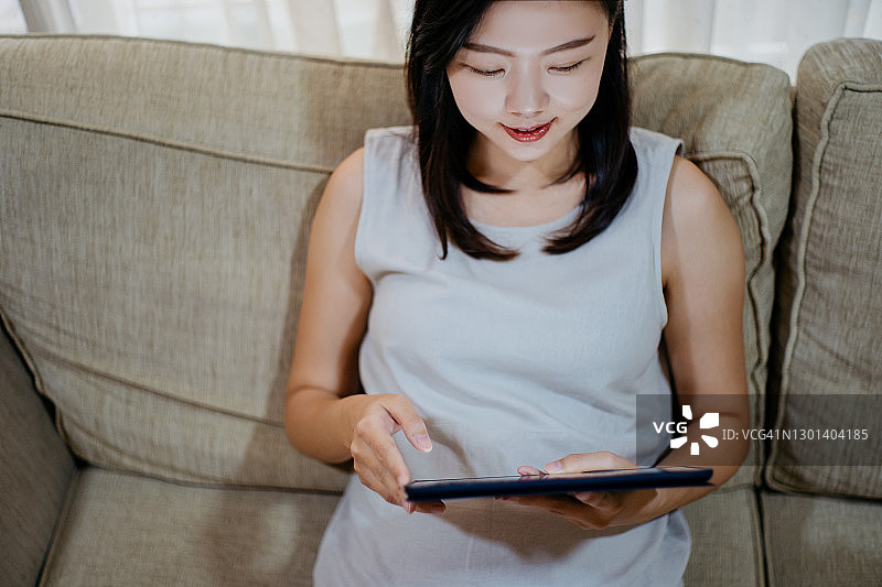年轻的亚洲女性在家里使用数字平板电脑图片素材