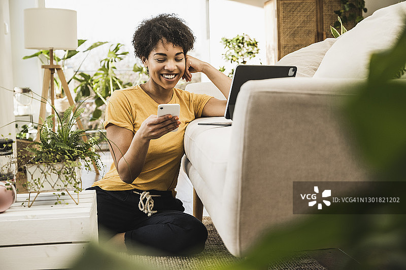 女人微笑着使用手机坐在家里的数字平板电脑图片素材