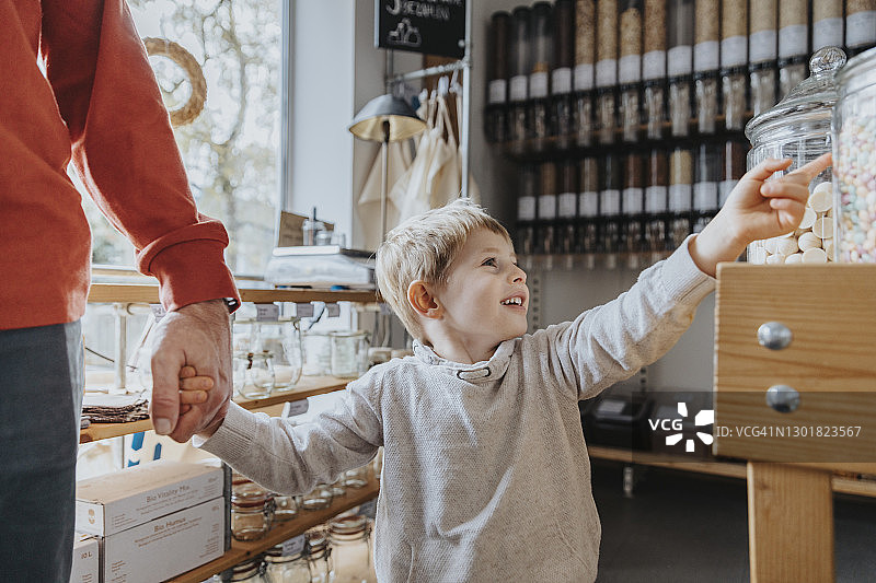 快乐的男孩牵着爸爸的手，指着店里的糖果罐图片素材