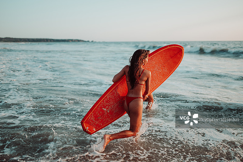 年轻女子带着冲浪板在海上奔跑图片素材