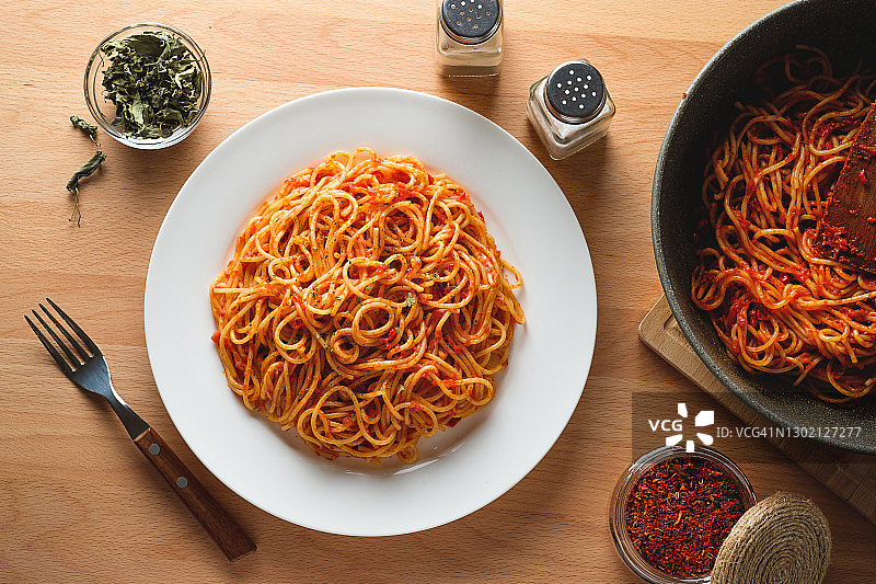 在厨房木桌子的背景下，陶瓷盘子上放着意大利面条或涂着番茄酱的肉酱面。在煎锅旁边，放着现成的菜。素食和素食食品的概念。食品的背景。图片素材