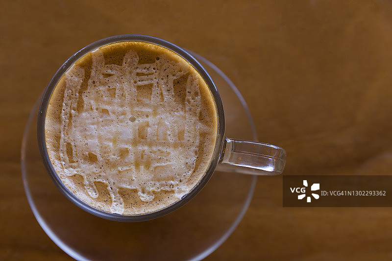 软焦点俯视图特写冰拿铁咖啡在一个白色的陶瓷杯在一个木头桌子的背景。聚焦选择性奶油玻璃顶部图片素材
