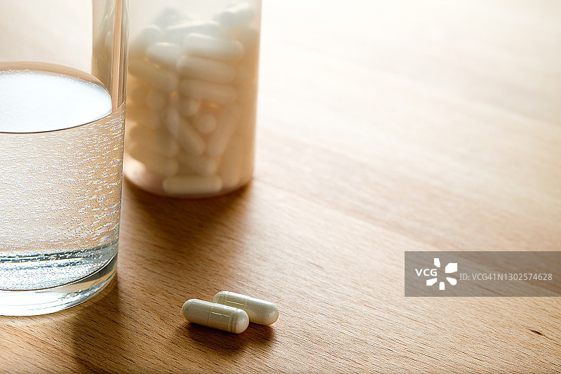 药片和一杯水放在厨房的木制桌子上。服用维生素、止痛药、药物和膳食补充剂。疾病的概念预防和治疗，保健和医药。计划和准备怀孕。图片素材