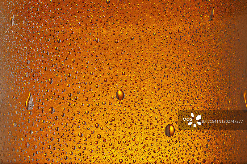 饮用玻璃-玻璃瓶上的凝结。冰啤酒杯与水滴橙色背景图片素材