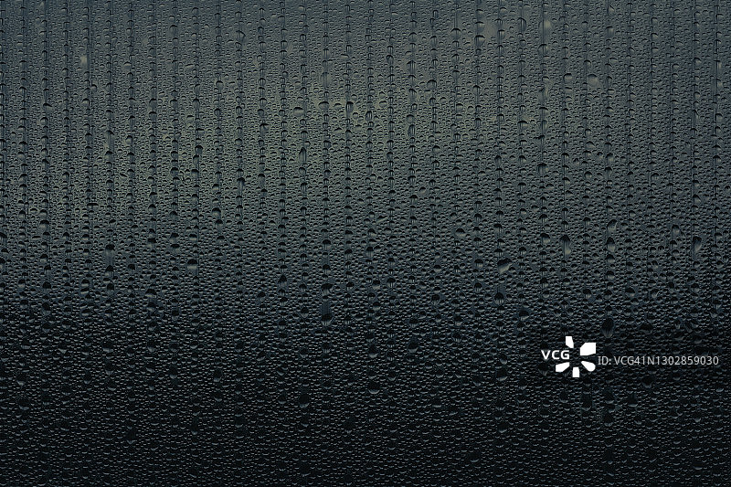 玻璃上一排一排流动的水滴构成的黑色背景。梯度斑点抽象图案。潮湿的平面结构图片素材