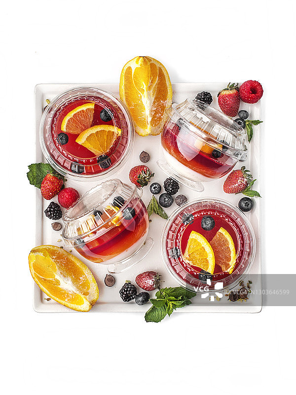 食物摄影的果冻和酸奶分层甜点与橙色水果和蓝莓近距离在一个封闭的塑料杯交付，顶部视图的白色背景孤立图片素材