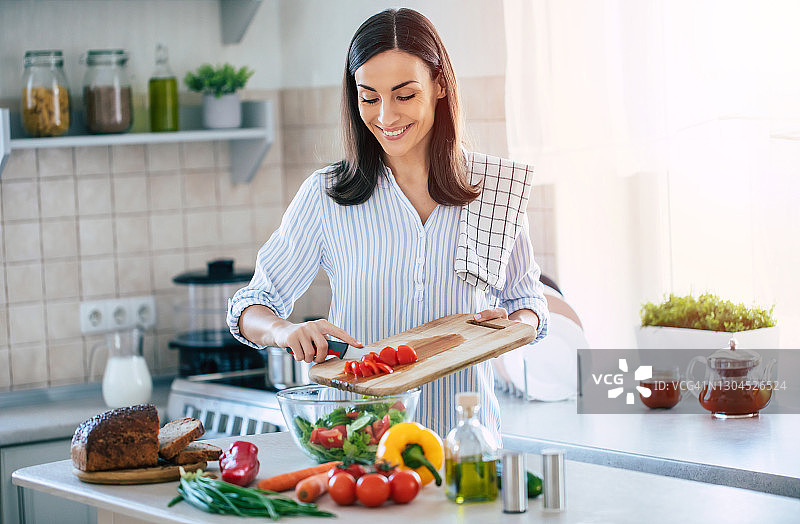 快乐微笑可爱的女人正在准备一个新鲜健康的素食沙拉与许多蔬菜在厨房在家里，并尝试一个新的食谱图片素材