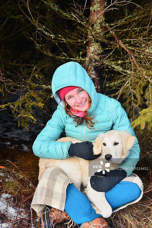 年轻女子拥抱她的金毛猎犬幼犬在松树林图片素材