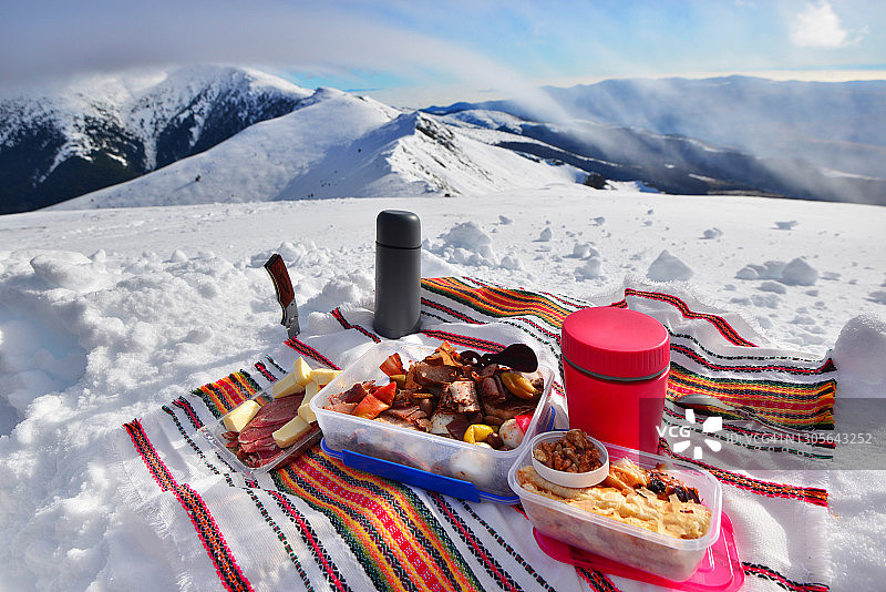 在白雪皑皑的山顶上野餐，欣赏美丽的山峰和白云图片素材