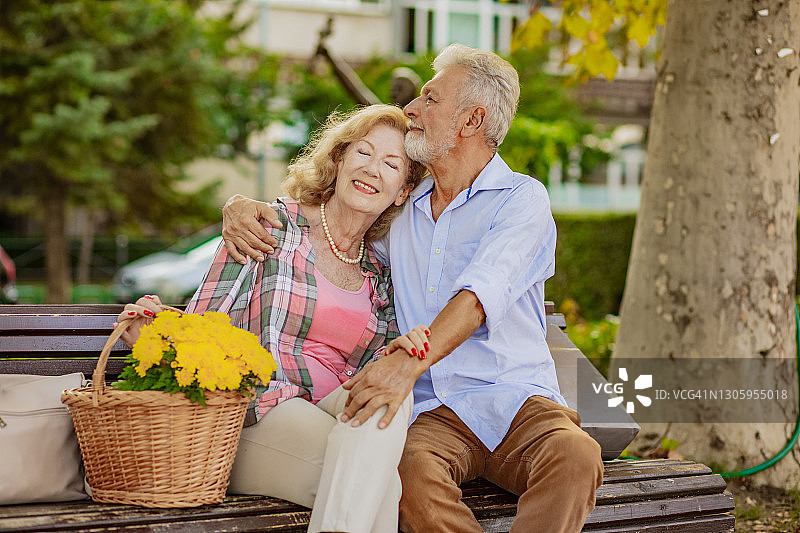 一对快乐的老年夫妇坐在公园的长椅上，面带微笑图片素材