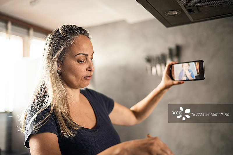 成熟的女人做饭和展示食物在视频通话在家里的智能手机图片素材