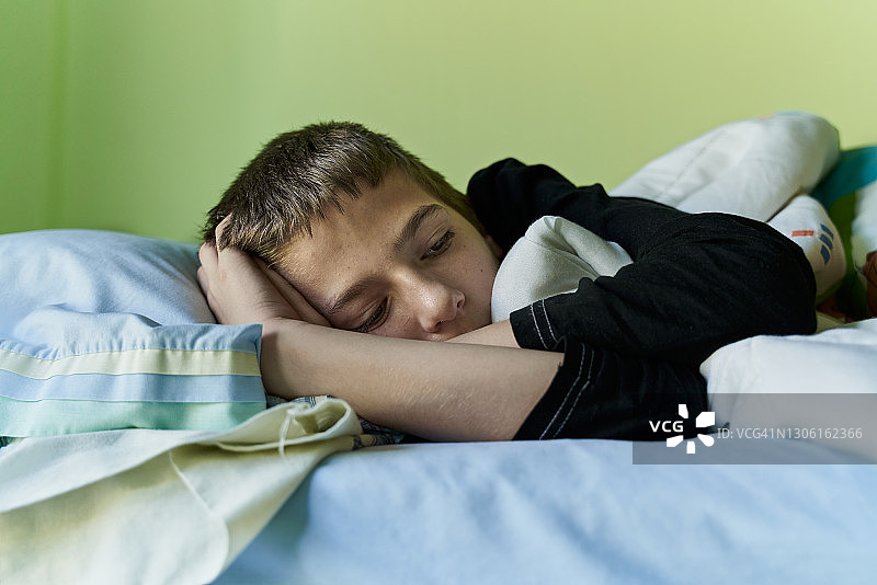 一个金发男孩蜷缩在床上，裹着毯子和床单。水平的照片图片素材