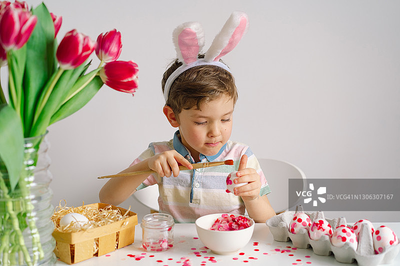 戴着兔子耳朵的小男孩装饰复活节彩蛋。图片素材