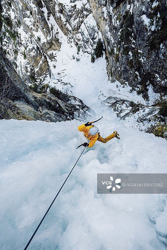 一名男性冰上攀登者正挥舞着冰镐在高处一个壮观的冰冻瀑布上俯视图片素材