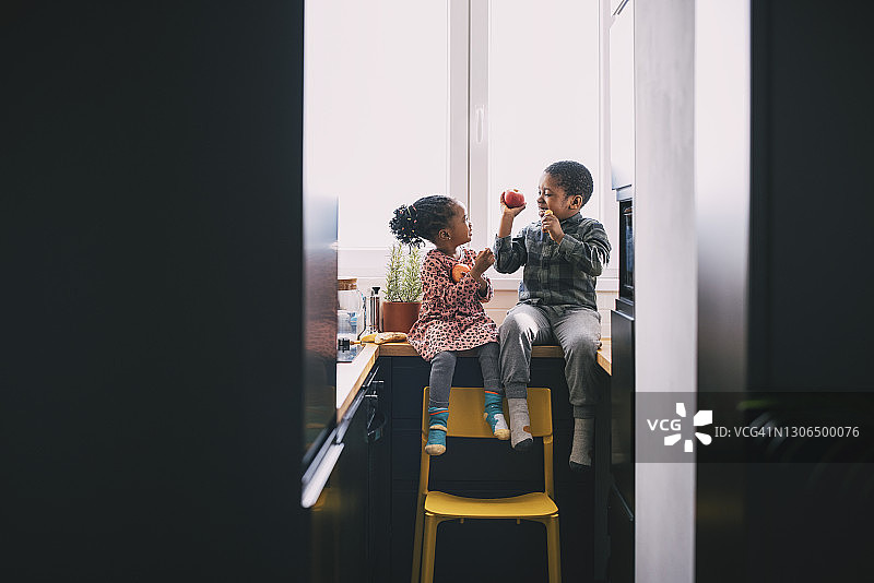 一个微笑的男孩和一个女孩坐在厨房柜台上吃水果图片素材