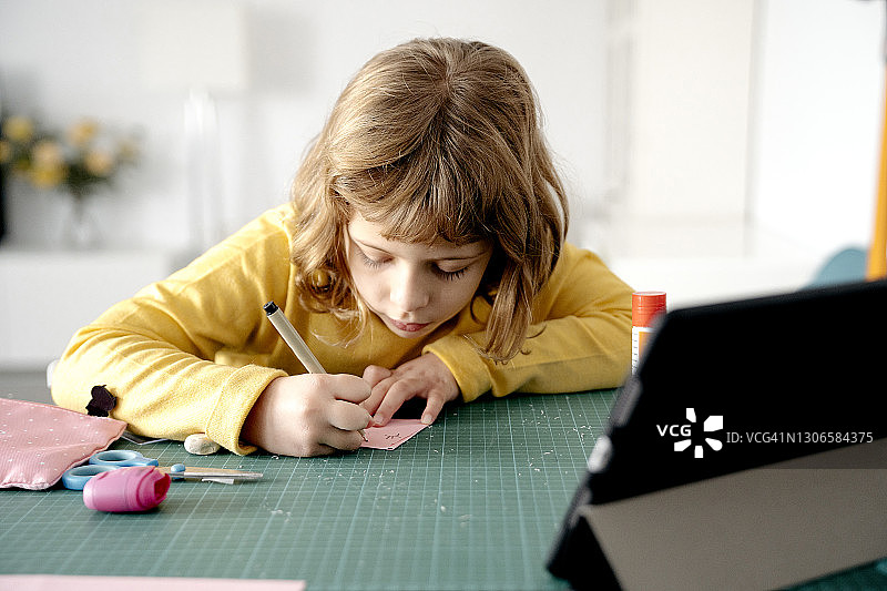 可爱的女孩在纸上画画，在桌上的数字平板电脑图片素材