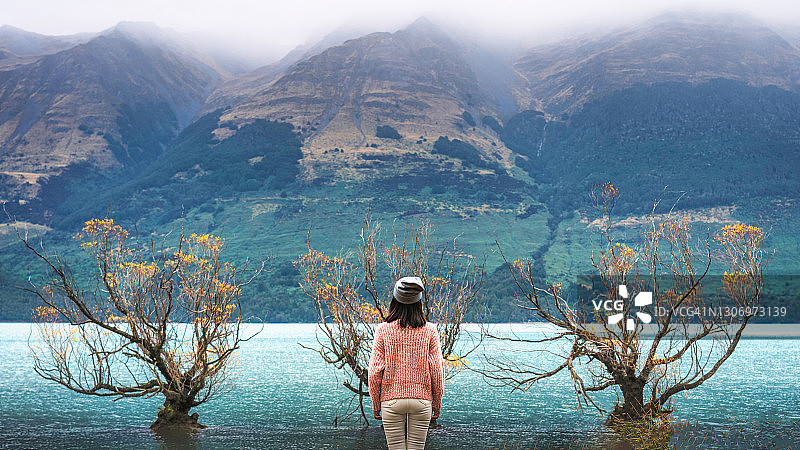 一位女士站在新西兰格勒诺奇的格勒诺奇湖旁。在新西兰奥塔哥地区，glenorchy的标志性柳树在日出时拍摄图片素材