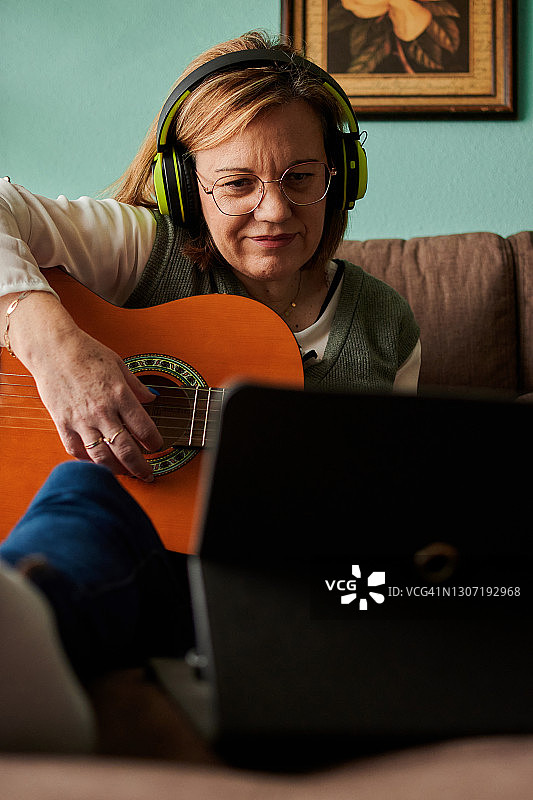 中年妇女戴着耳机坐在家里的沙发上弹吉他图片素材