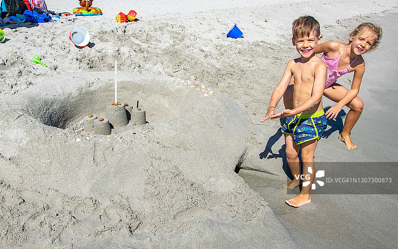 快乐和顽皮的男孩和女孩在沙滩上制造沙堡图片素材