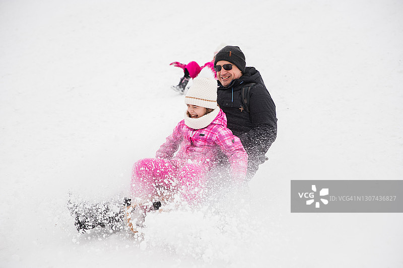 快乐的女孩在雪和她的父母玩图片素材