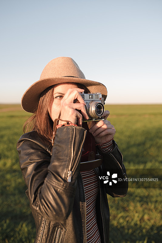 一个农村年轻女子的垂直肖像。她走在户外，用她的老式模拟相机拍照。电影摄影师。图片素材