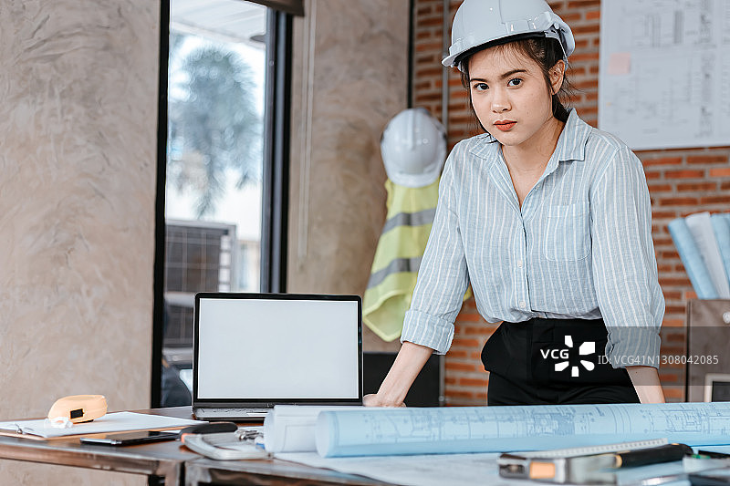 工地施工现场，建筑女工在桌子上阅读设计图，戴上安全帽。建筑、工程、商业和民用概念。图片素材