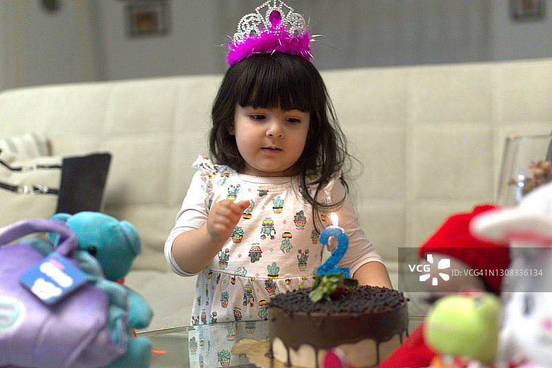可爱的两岁生日女孩盯着蜡烛的巧克力蛋糕图片素材