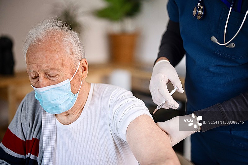 老人戴着防护口罩在家接种疫苗图片素材