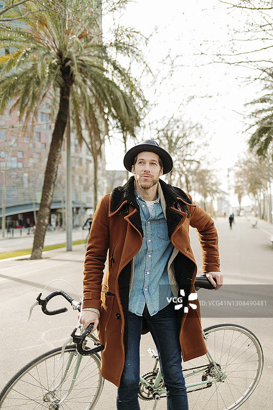 一名戴着帽子的男子骑着自行车站在城市的道路上图片素材