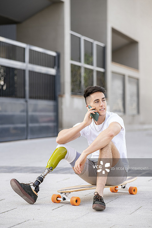 一个年轻的残疾人坐在滑板上用手机打电话图片素材