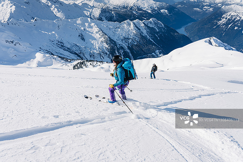 两名滑雪者站在冰川上，上面是一个深深的海岸山谷和湖泊图片素材