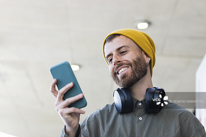 微笑的男人与针织帽使用智能手机，而站在户外图片素材
