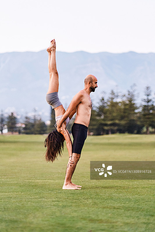 一对情侣在公园里一起做瑜伽倒立图片素材
