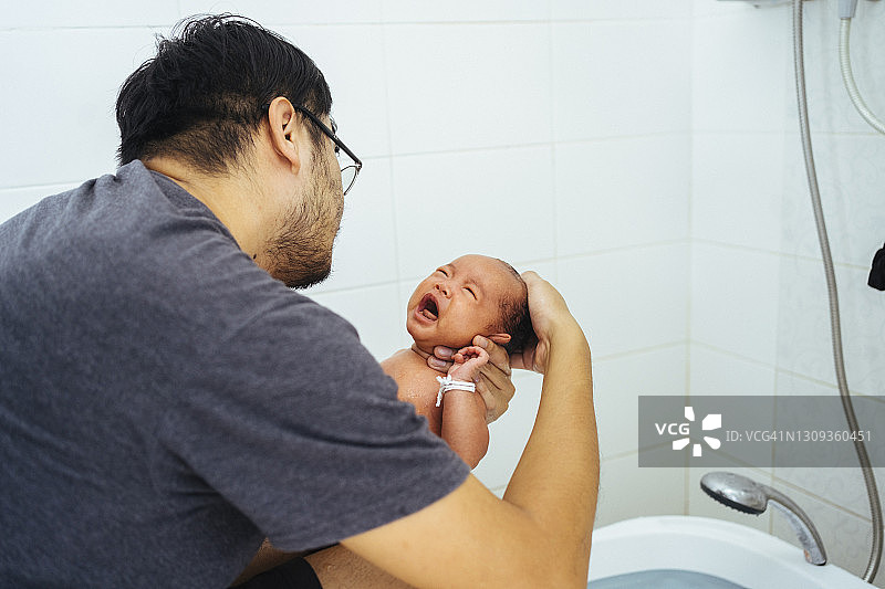 亚洲年轻的成年父亲在家里的浴室里为他的小女儿洗澡图片素材