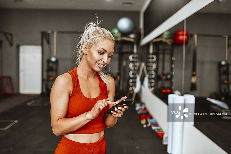 微笑的金发女运动员用智能手机在健身房寻找新的锻炼方式图片素材