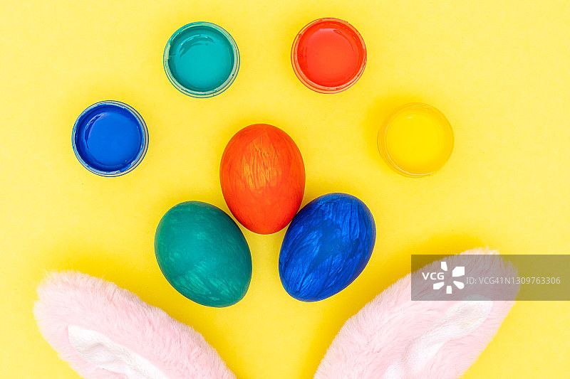 复活节快乐的概念。复活节布置:五彩缤纷的彩蛋，颜料，粉红色的兔子耳朵上亮黄色的背景图片素材