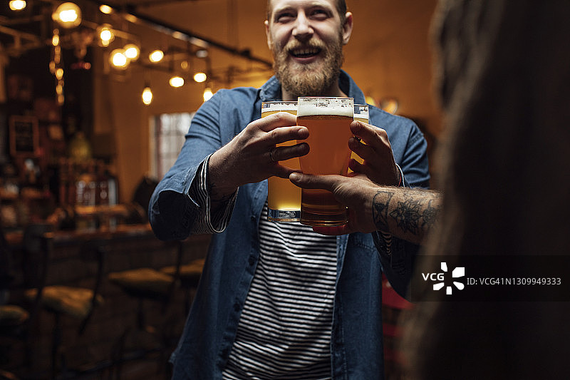 快乐的金发嬉皮士在酒吧给他的朋友带啤酒图片素材
