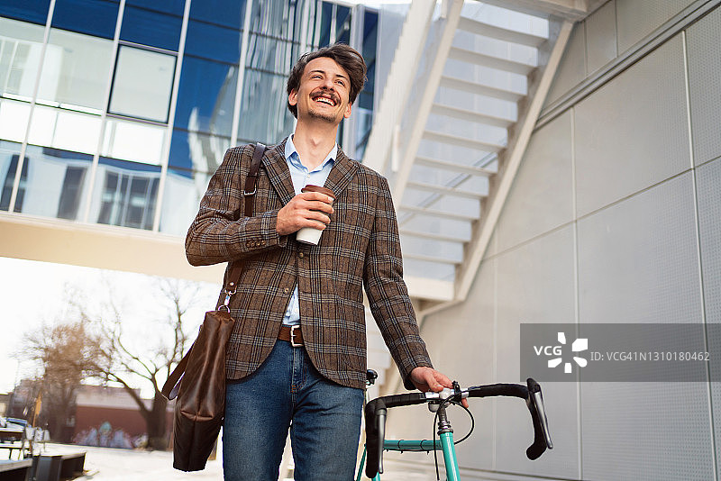低角度的一个微笑的商人与一杯咖啡和自行车去工作图片素材