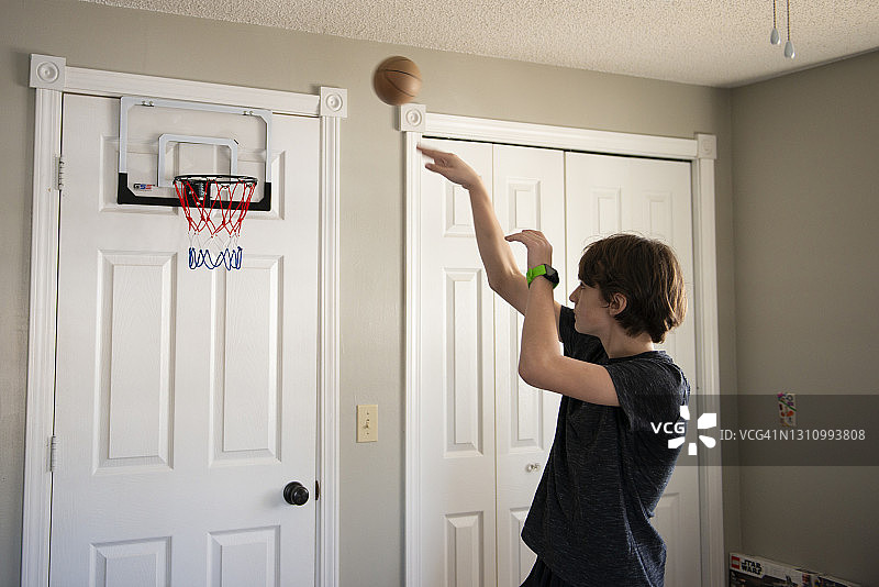 小男孩在卧室里扔小篮球。图片素材