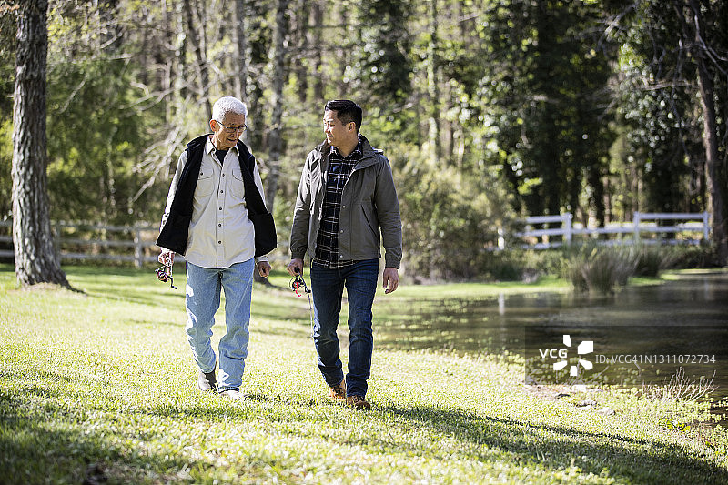 年长的父亲和成年的儿子带着渔具在农场湖边散步图片素材