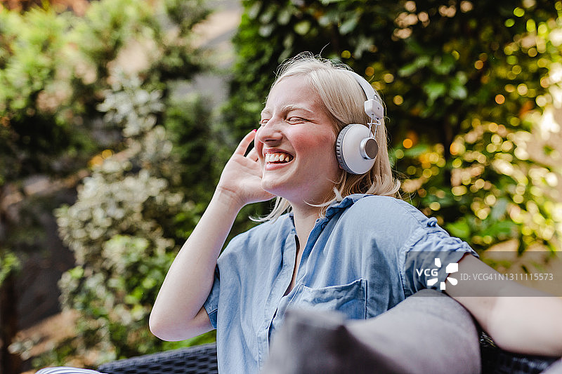 一个年轻女子戴着耳机在阳台上听着轻松的音乐图片素材