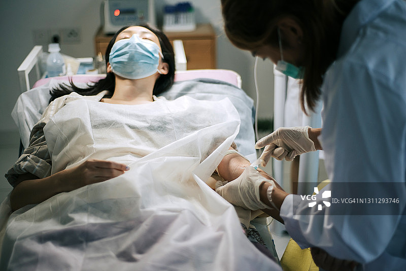 一名亚裔华人女护士在诊所为女性华人病人的手静脉采血图片素材