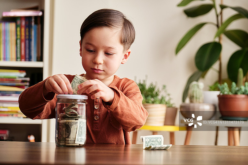 孩子在家里用玻璃罐子存钱图片素材