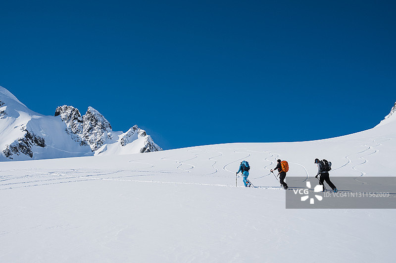 3个人排成一排，沿着冰川滑雪图片素材