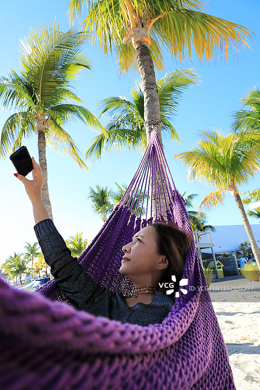 美丽的女人自拍和放松在热带沙滩上的吊床图片素材