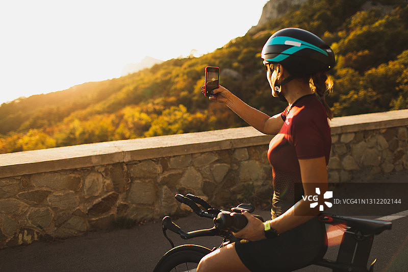 一个女人在户外骑自行车，用智能手机拍下美丽的日落图片素材