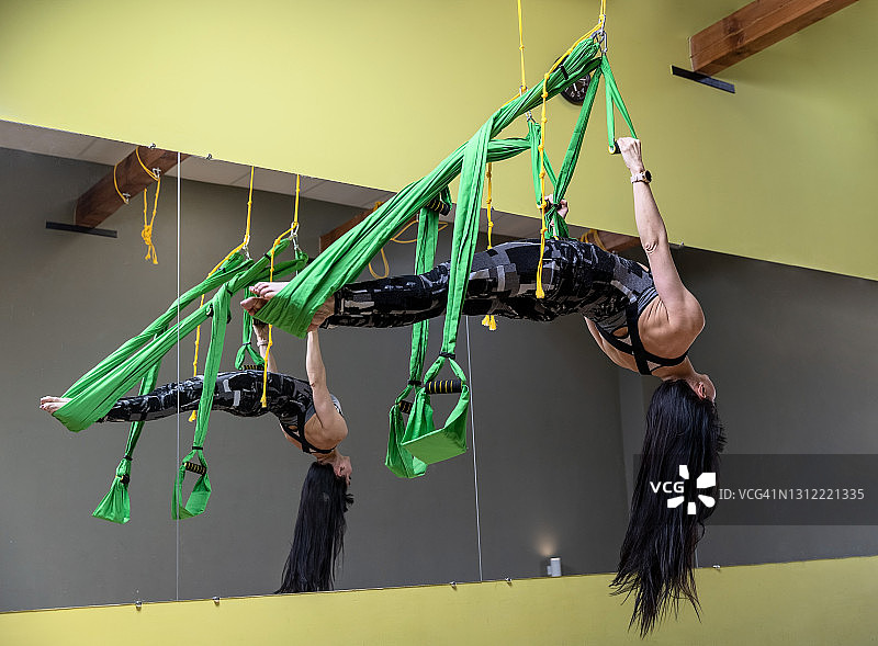 女性在室内练习空中反重力瑜伽，用吊床和带子倒挂。图片素材